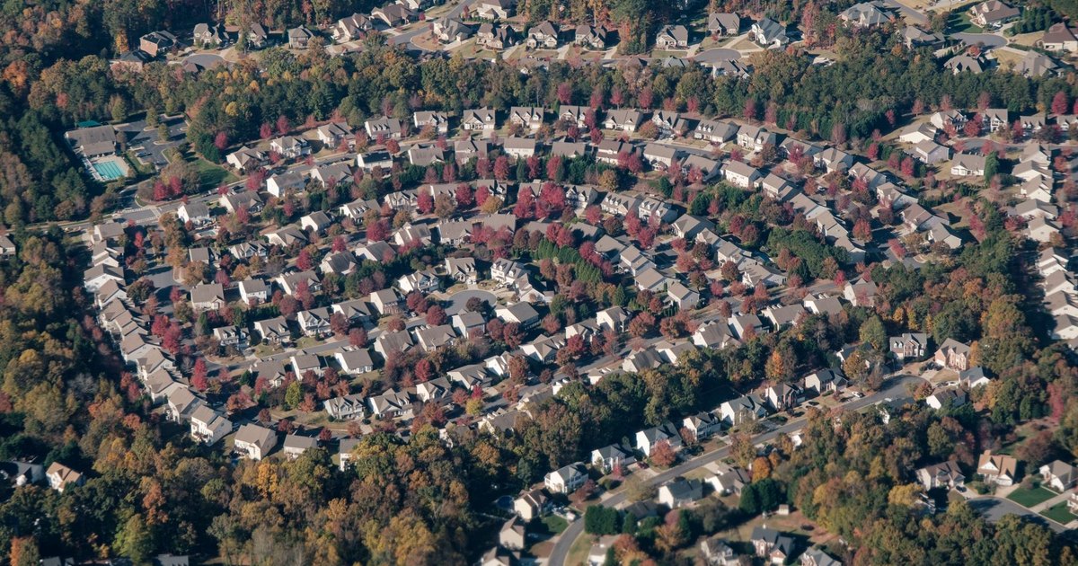 Aerial view of a curving suburban subdivision of homes surrounded by autumn trees