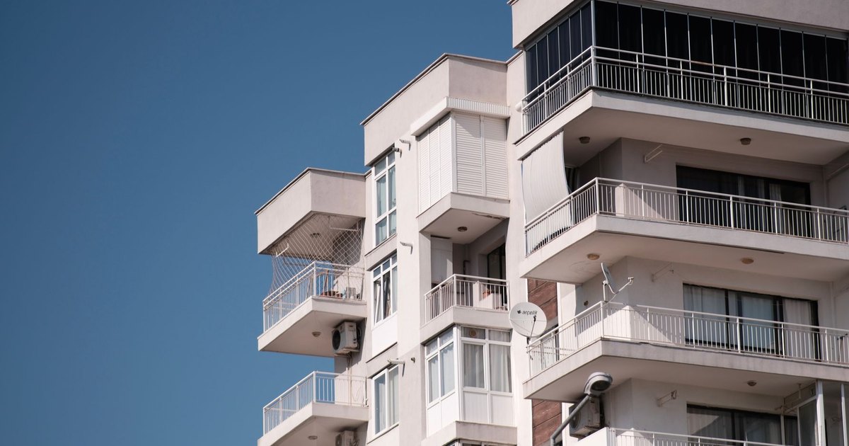 White multi-story condo building with stacked balconies against a clear blue sky